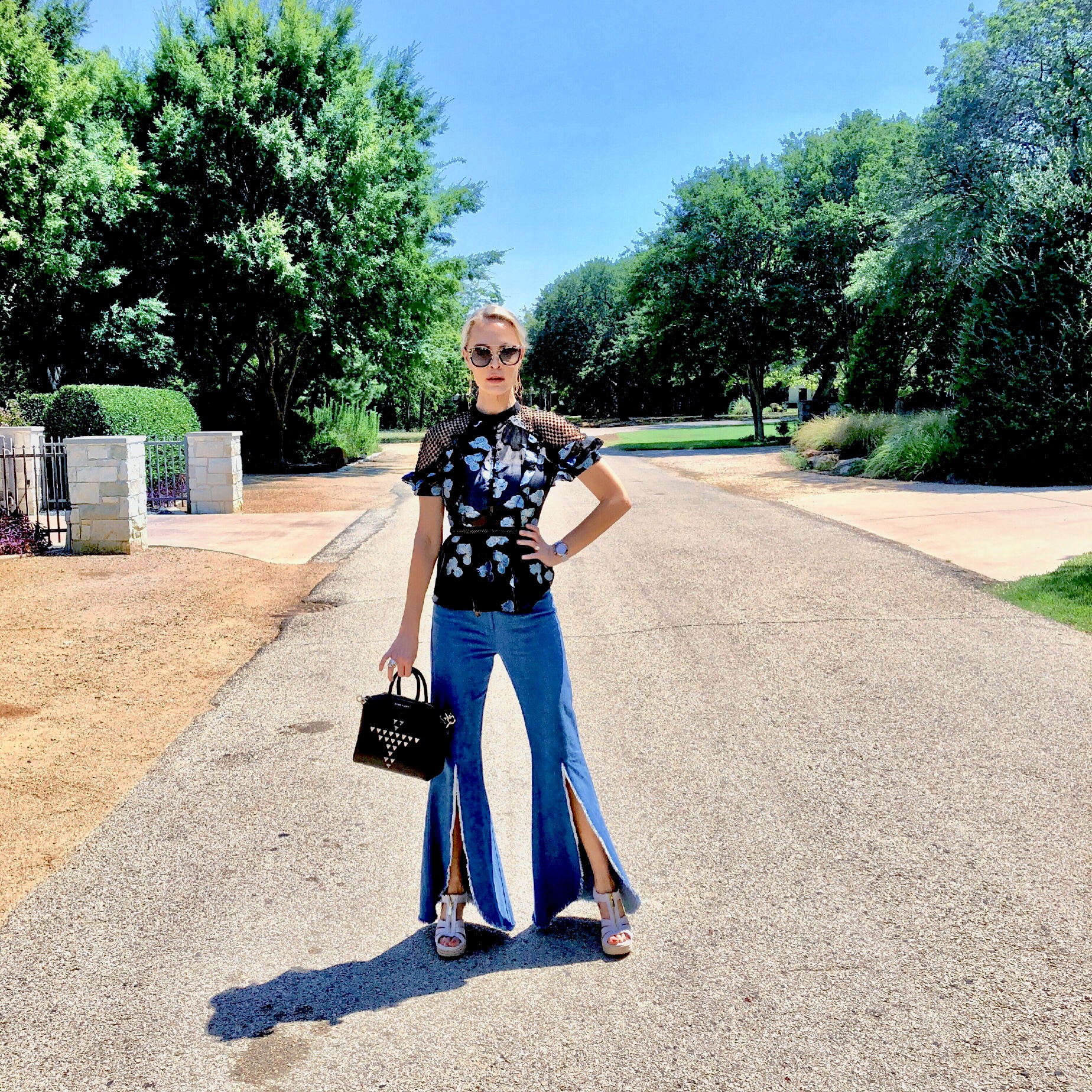 posing with a studded black purse and flared jeans