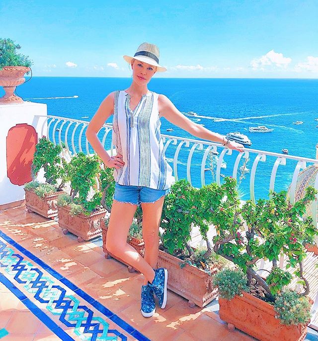 Whitney on a balcony in front of the ocean wearing a striped tank and denim shorts